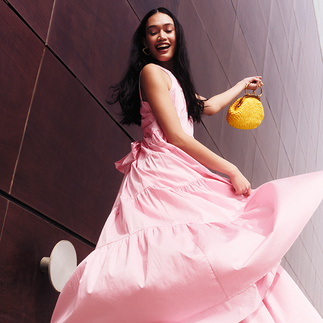 Model wearing a long pink dress with a yellow bag