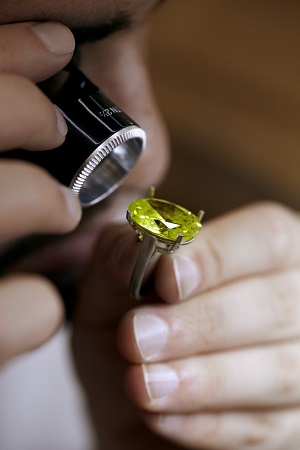 A person examining with a magnifying glass a ring with a gemstone