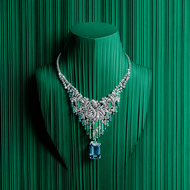 A necklace with diamonds, green gemstones and one big blue gemstone