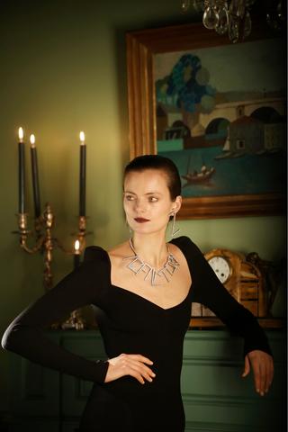 A woman model wearing a black dress with long sleeves, a necklace and earrings