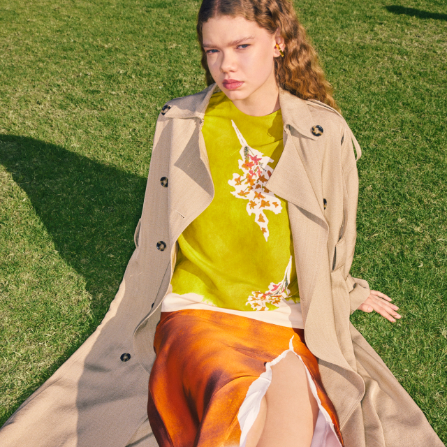 Model wearing a beige trenchcoat sitting on the grass